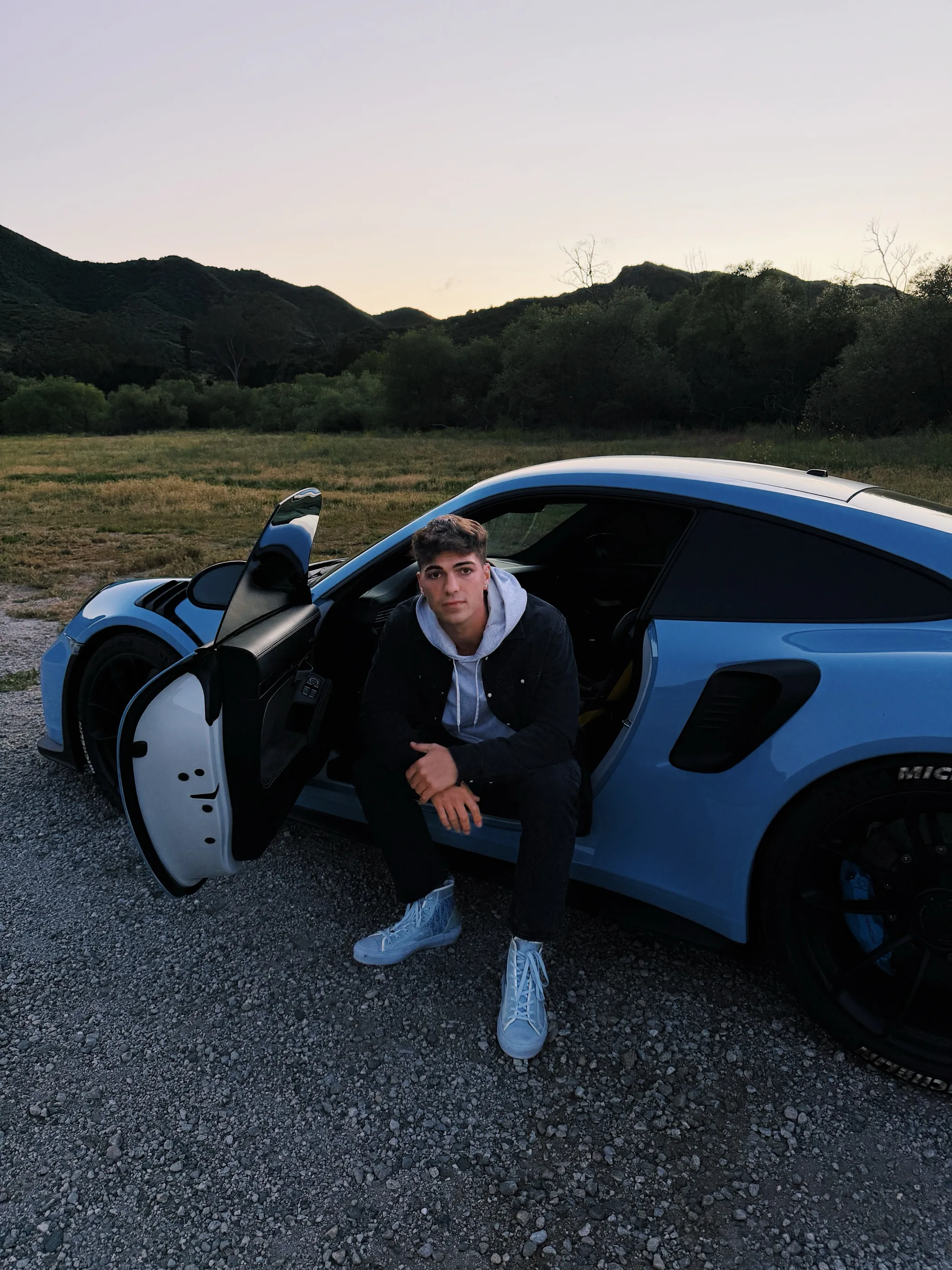 Thomas sitting in the doorway of a blue Porsche 911 GT3 RS at dusk