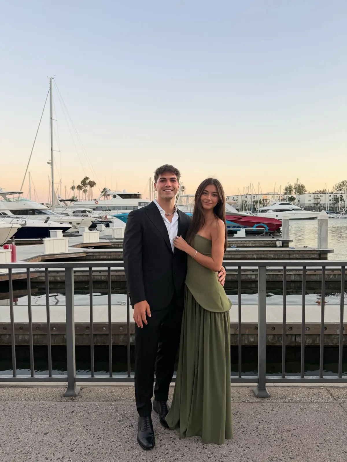 Thomas in a black suit at a marina at sunset